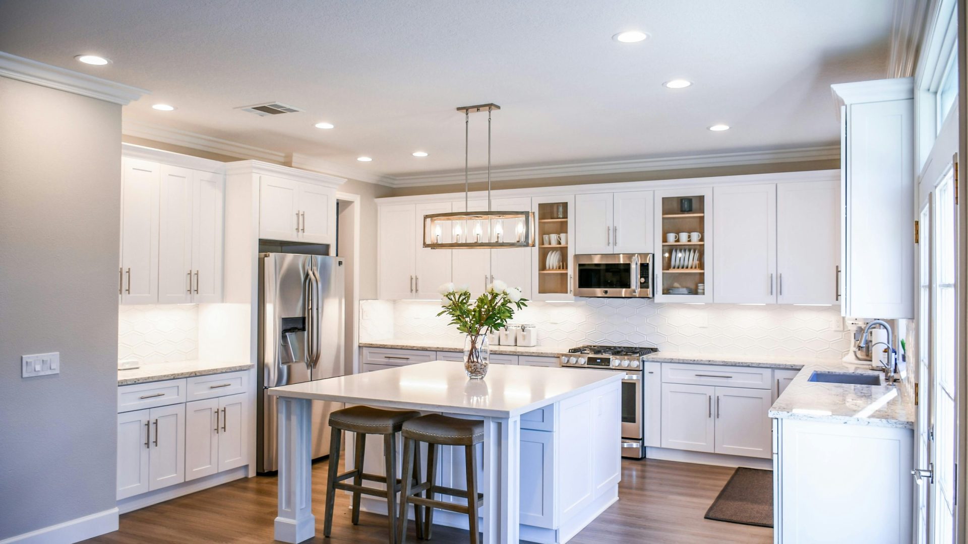 Elegant white kitchen featuring an island, modern appliances, and ample natural light.