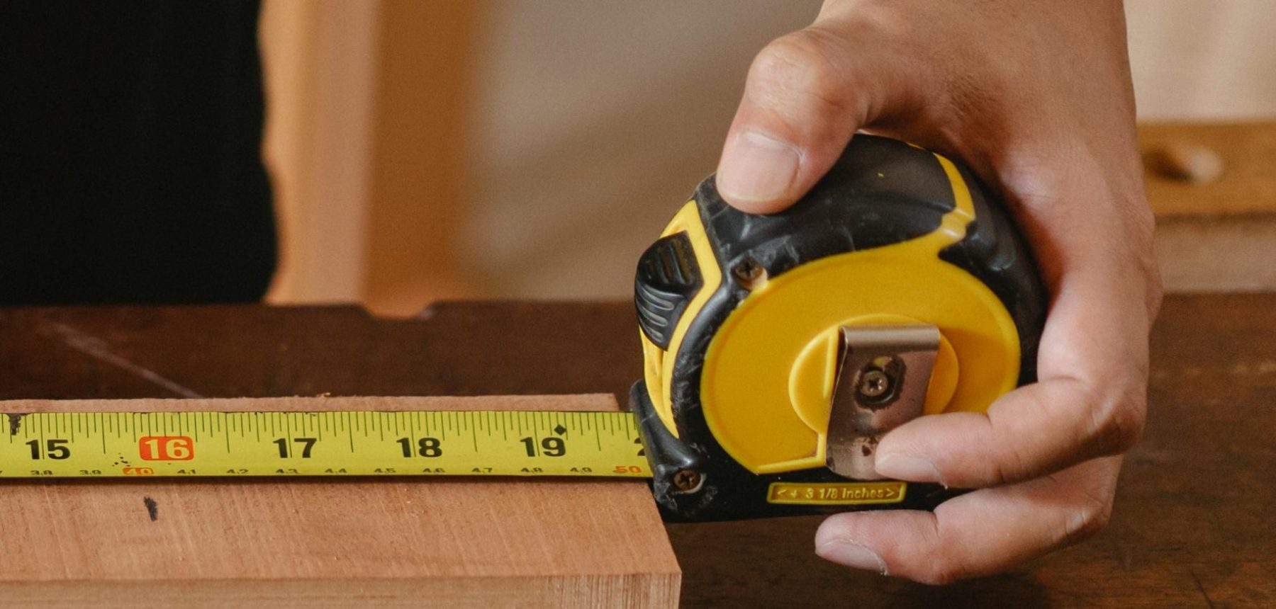 Close-up of carpenter's hand measuring wood with a tape measure in a workshop.