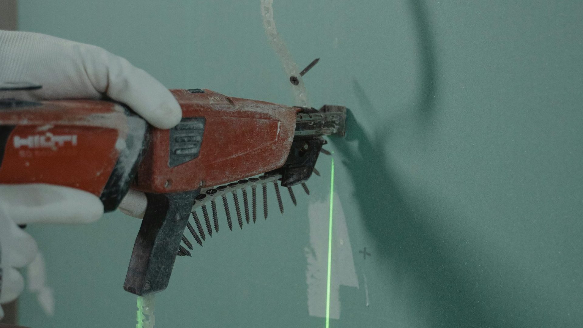 Close-up of a handyman using a laser level and nail gun for drywall installation.