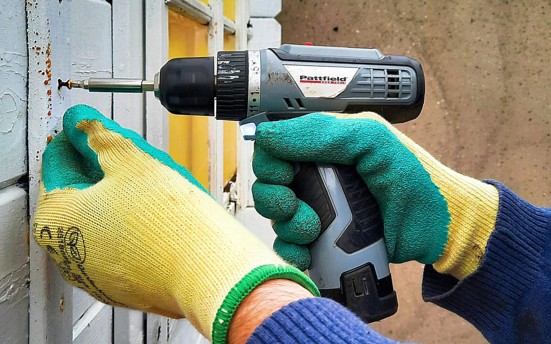 Close-up of a construction worker using a drill on a wooden wall, focusing on hands and tool.